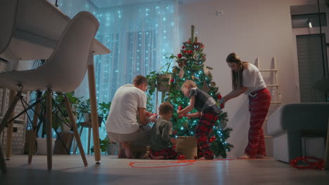 A-family-with-two-children-decorate-a-Christmas-tree-on-Christmas-Eve.-Father-and-mother-with-children-prepare-for-new-year-and-Christmas-decorating-house.-High-quality-4k-footage